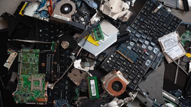 Kaputte Computerteile wie Festplatten, Tastatur und Laufwerke liegen auf einem Tisch.