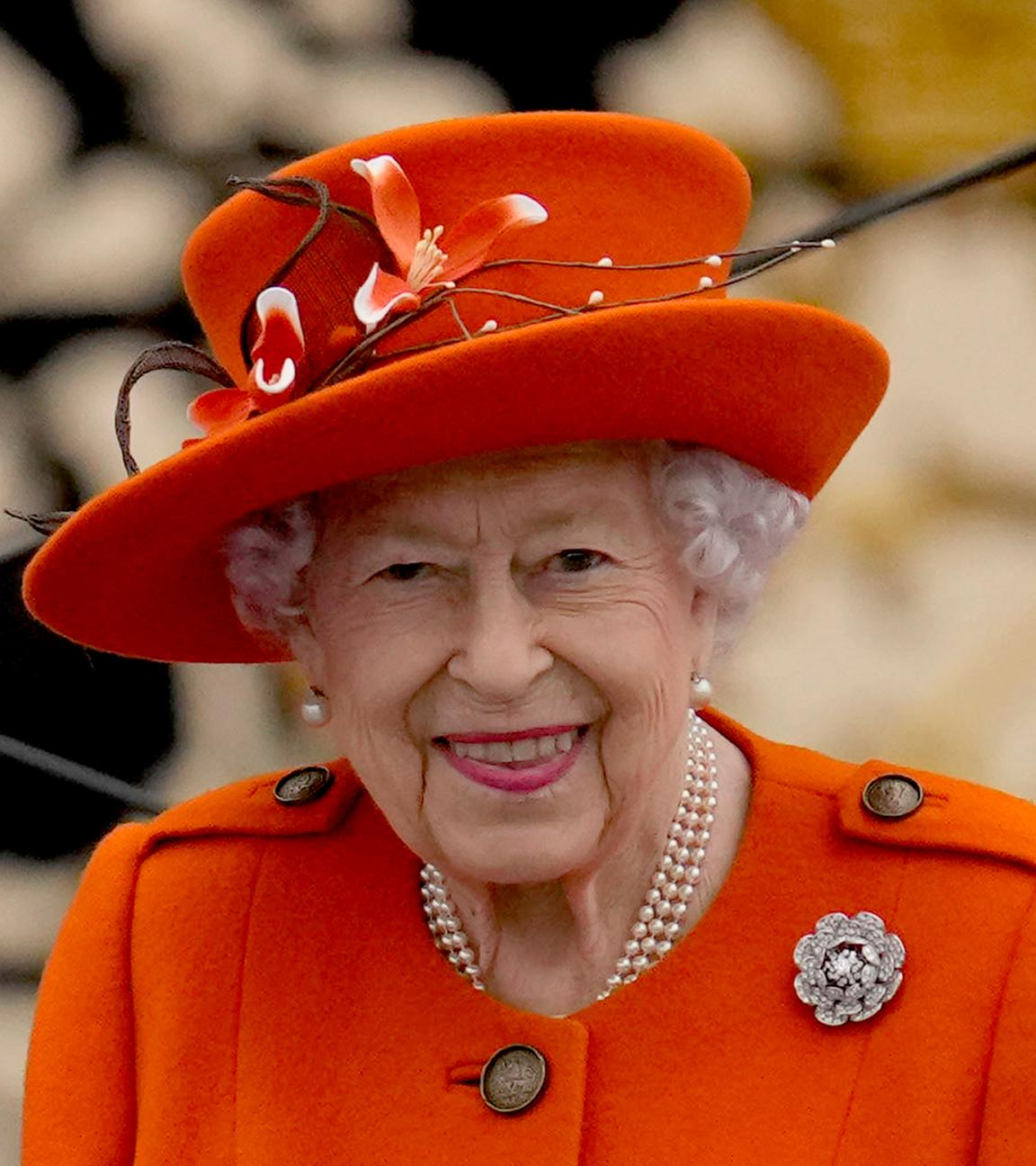 Königin Elizabeth II. lachend in einem orangefarbenen Outfit.