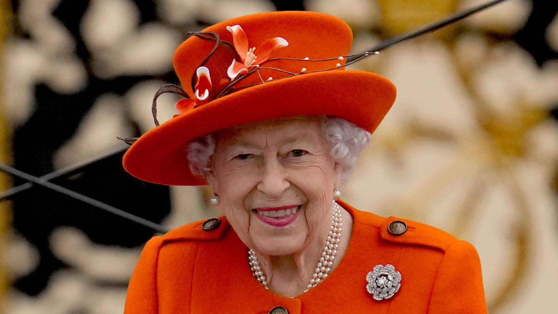 Königin Elizabeth II. lachend in einem orangefarbenen Outfit.