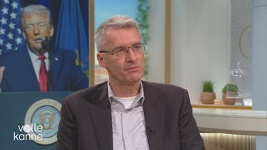 ZDF-Journalist Elmar Theveßen im Volle-Kanne-Studio. Im Hintegrund ein Foto von Donald Trump.
