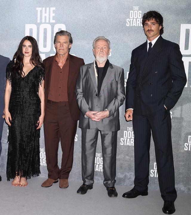 Das Bild zeigt sechs Schauspieler bei einer Premiere vor einer Fotowand mit dem Schriftzug „The Dog Stars“. Die Hollywood Stars posieren gemeinsam für Fotos und tragen elegante Abendgarderobe und Anzüge.