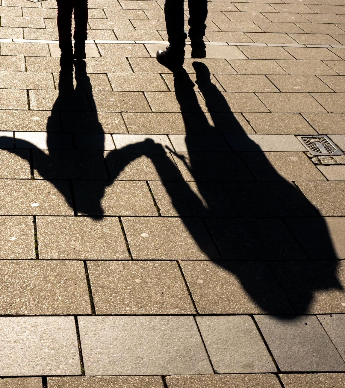 Die Schatten von zwei Erwachsenen und einem Kind sind in den Morgenstunden auf dem Asphalt in der Innenstadt zu sehen.