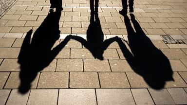 Die Schatten von zwei Erwachsenen und einem Kind sind in den Morgenstunden auf dem Asphalt in der Innenstadt zu sehen.