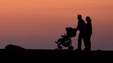 Ein Pärchen mit Kinderwagen geht in der Abenddämmerung spazieren (Symbolfoto)