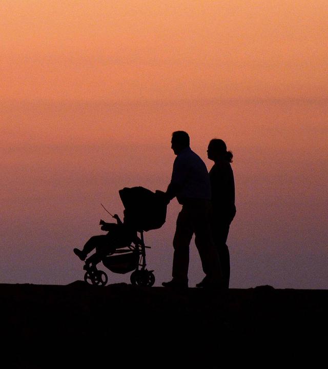 Ein Pärchen mit Kinderwagen geht in der Abenddämmerung spazieren (Symbolfoto)