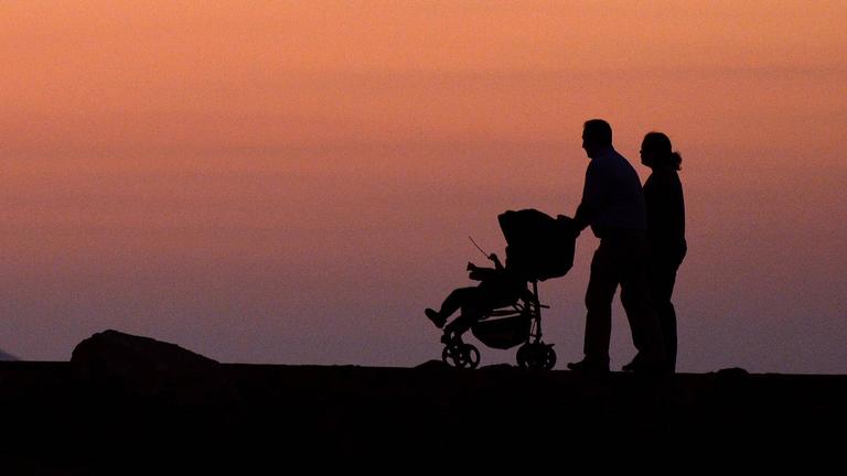 Ein Pärchen mit Kinderwagen geht in der Abenddämmerung spazieren (Symbolfoto)