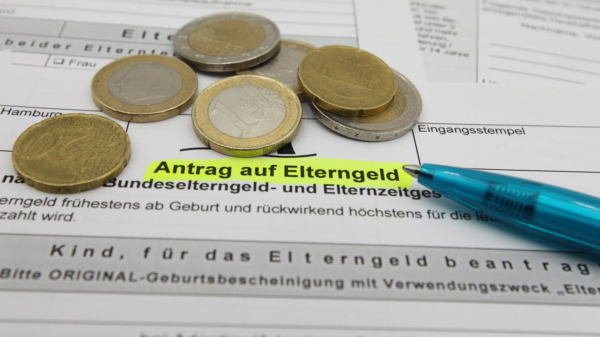 Ein Antrag auf Elterngeld, ein Kugelschreiber sowie Euro-Münzen liegen auf einem Schreibtisch. 