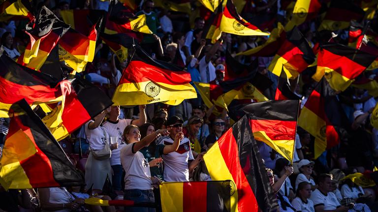 Deutsche Fans jubeln und schwenken Fahnen bei der Fußball EM der Frauen.