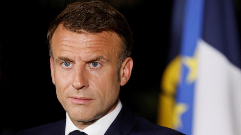 Der französische Präsident Macron steht vor einem schwarzen Hintergrund und schaut mit ernster Miene in die Ferne.