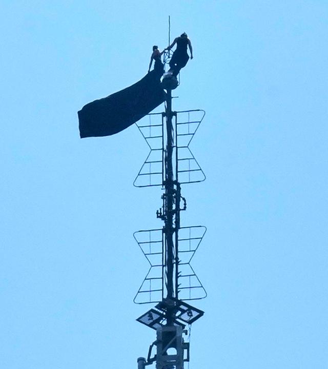 Zwei Menschen stehen auf der Spitze der Antenne des Empire State Building und halten ein Transparent hoch.