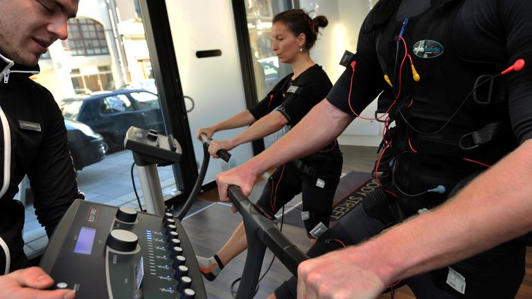 Zwei Personen mit Weste und Elektroden werden beim EMS-Training im Fitnesstudio angeleitet.