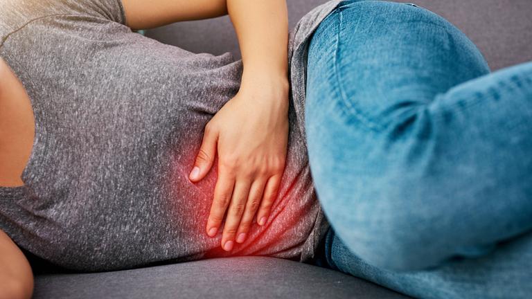 Eine Frau liegt auf der Seite und hält sich den schmerzenden Bauch.