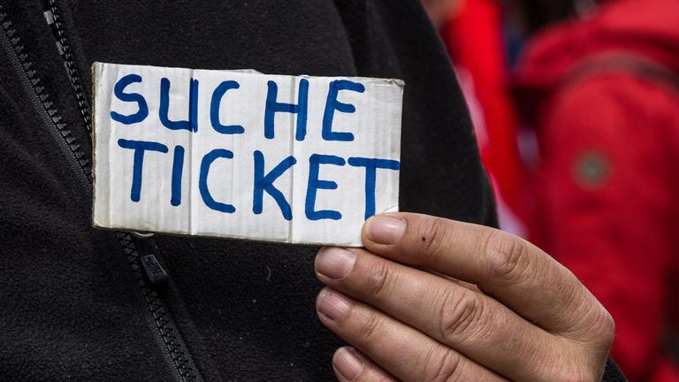 "Suche Ticket" steht auf einem Schild, das ein Besucher am Eingang zum Stadion hält