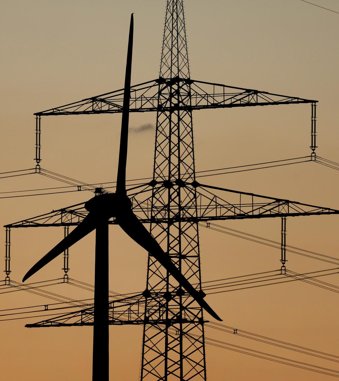 Die Spitzen eines Strommasts und eines Windrades vor orangenem Himmel.