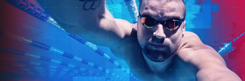 Unterwasseraufnahme des Schwimmers Marius Kusch im Becken während des Trainings. Der ehemalige Olympia-Sportler trägt eine Schwimmbrille und streckt den Arm nach vorn in Richtung Kamera. Auf dem Oberarm ist ein Tattoo mit olympischen Ringen zu sehen. Im Hintergrund verlaufen die Leinenbahnen des Pools, das Bild ist in kräftigen Blau- und Magentatönen gestaltet, zudem ist ein grafisches Raster-Overlay sichtbar.