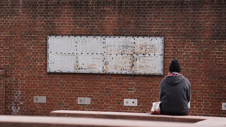 Eine Person sitzt vor dem Presidential House in Philadelphia vor einer Wand von der ein Teil der Open Air Ausstellung gegen Sklaverei in den USA entfernt wurde.