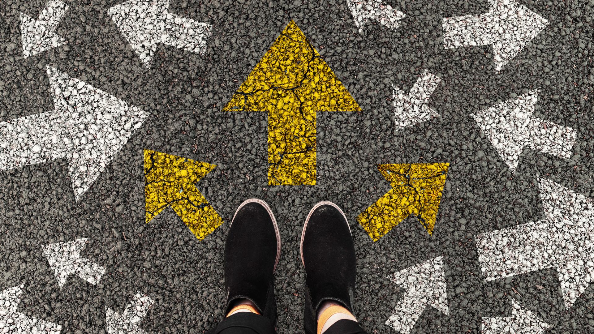 Eine Person steht auf einer Straße auf der mehrere Pfeile in verschiedene Richtungen weisen.