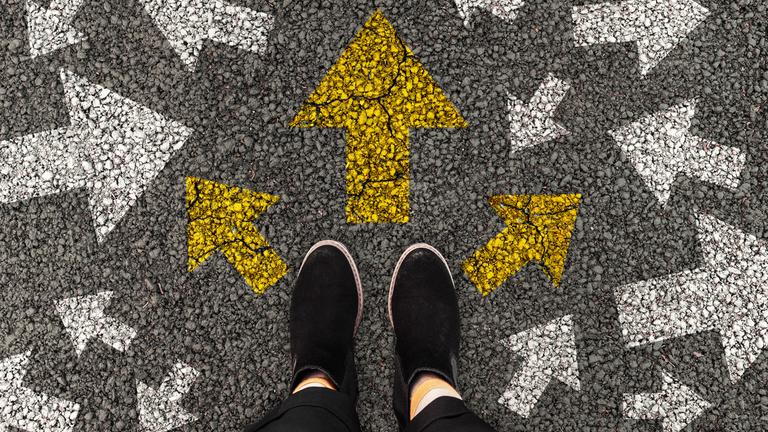 Eine Person steht auf einer Straße auf der mehrere Pfeile in verschiedene Richtungen weisen.