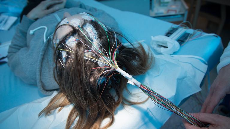 Person mit EEG-Sensoren auf dem Kopf liegt auf einem Krankenbett.
