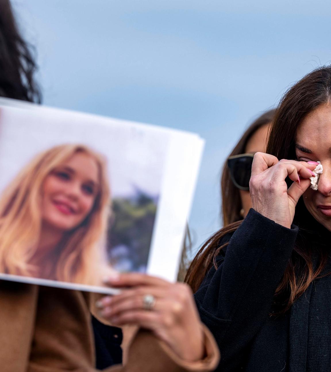 Eine Frau mit langen dunklen Haaren wischt sich mit einem Taschentuch die Tränen aus den Augen, während eine zweite das Foto einer jungen blonden Frau hoch hält.