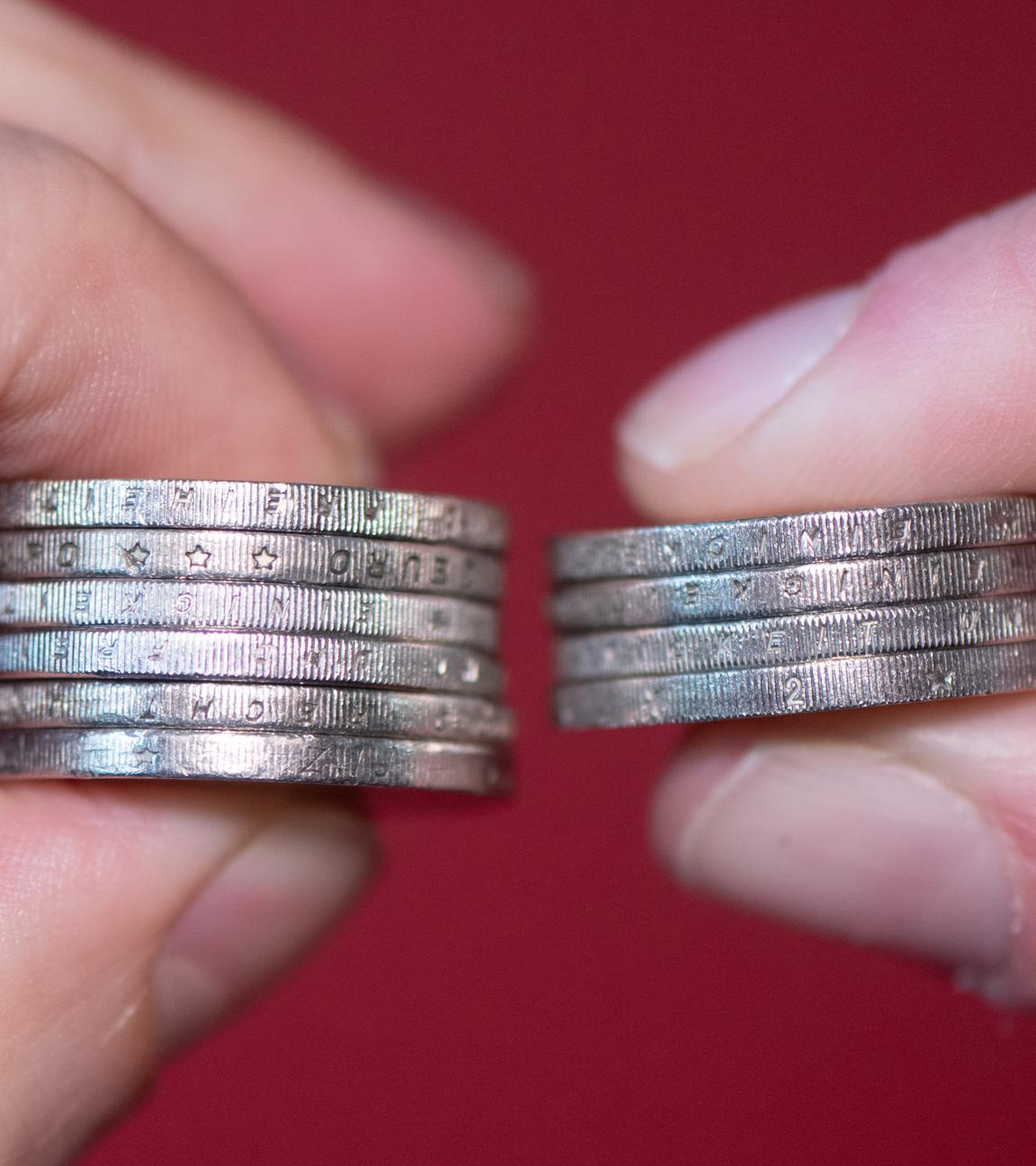 in Mann und eine Frau halten gestapelte Zwei-Euro-Münzen zwischen Daumen und Zeigefinger.
