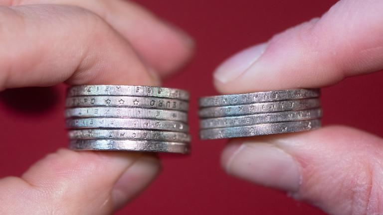 in Mann und eine Frau halten gestapelte Zwei-Euro-Münzen zwischen Daumen und Zeigefinger.
