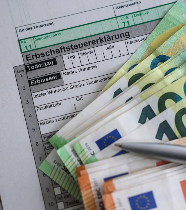 Sachsen, Leipzig: Auf einem Bogen zur Erbschaftsteuererklärung liegen Geldscheine von 100 und 50 Euro.