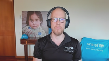 Gabriel Vockel von UNICEF Deutschland. Er hat ein schwarzes Polo-Shirt von UNICEF an und im Hintergrund ist eine hellblaue UNICEF-Tasche zu sehen.