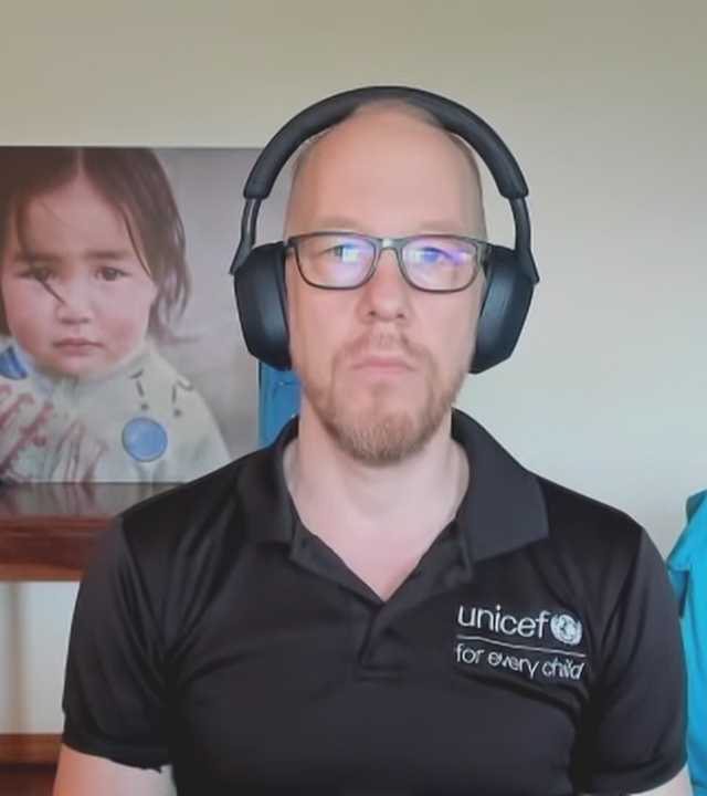 Gabriel Vockel von UNICEF Deutschland. Er hat ein schwarzes Polo-Shirt von UNICEF an und im Hintergrund ist eine hellblaue UNICEF-Tasche zu sehen.