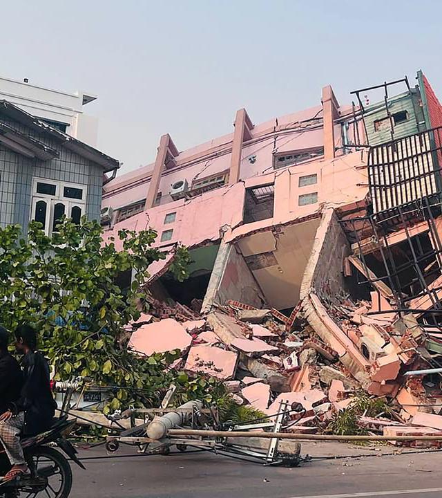 Menschen fahren am 28. März 2025 nach einem Erdbeben in Zentralmyanmar auf einem Motorrad an einem eingestürzten Gebäude in Mandalay vorbei.