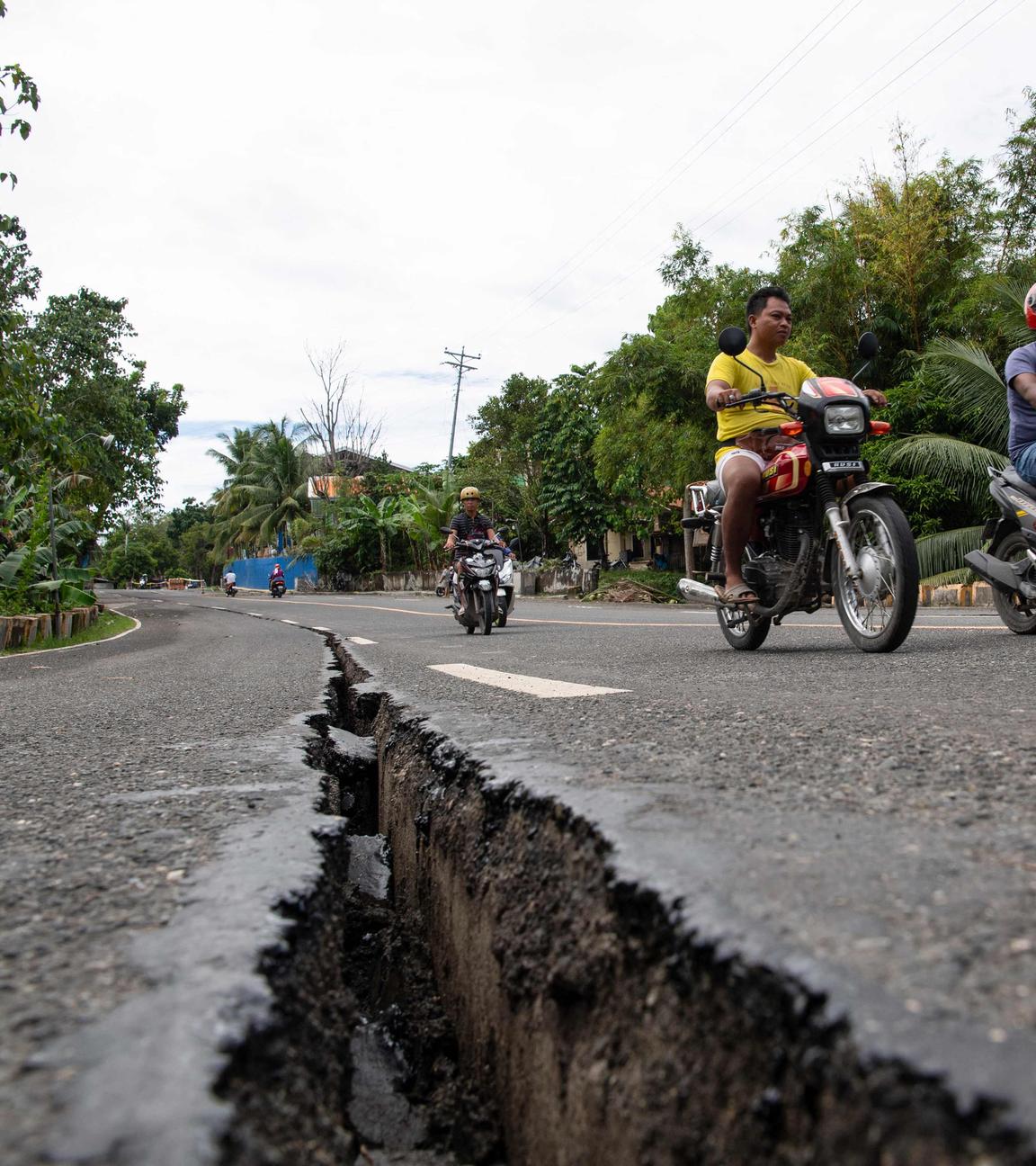 Motorräder fahren über eine Straße in den Philippinen, durch die nach einem Erdbeben ein breiter Riss geht.