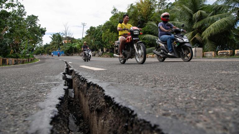Motorräder fahren über eine Straße in den Philippinen, durch die nach einem Erdbeben ein breiter Riss geht.