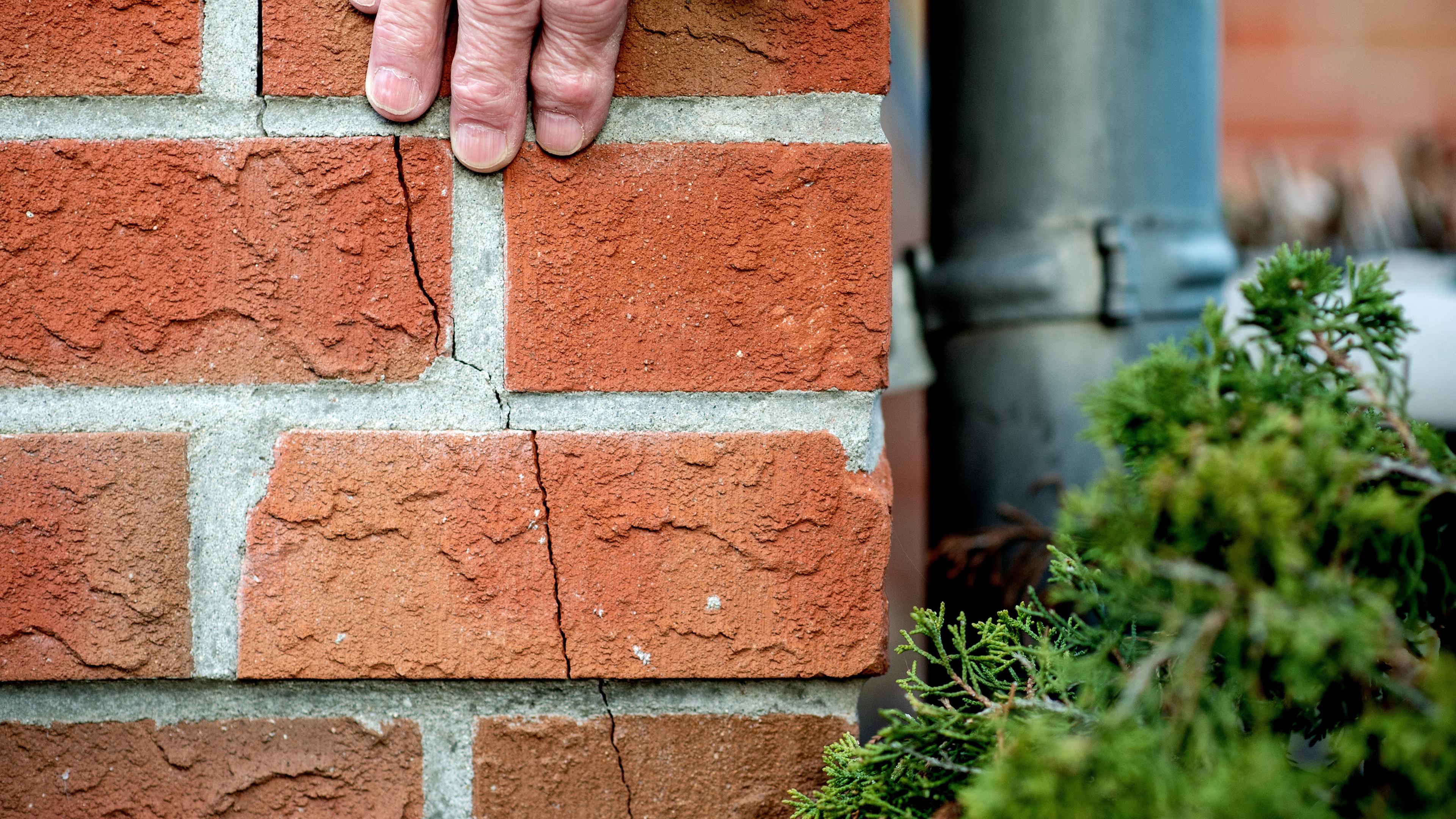Niedersachsen, Dörverden: Ein Mann streicht mit seiner Hand über den durch ein Erdbeben entstanden Riss am Haus im Ortsteil Stedebergen. Archivbild