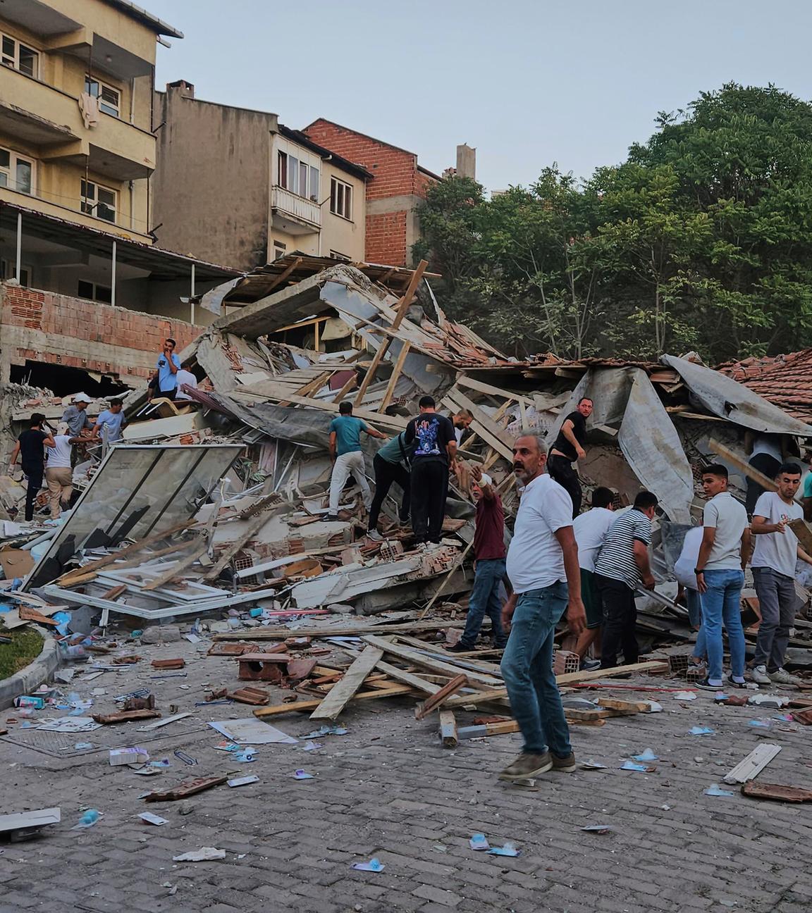 10.08.2025, Türkei, Sindirgi: Menschen beseitigen die Trümmer eines eingestürzten Gebäudes nach einem Erdbeben in Sindirgi in der Westtürkei.