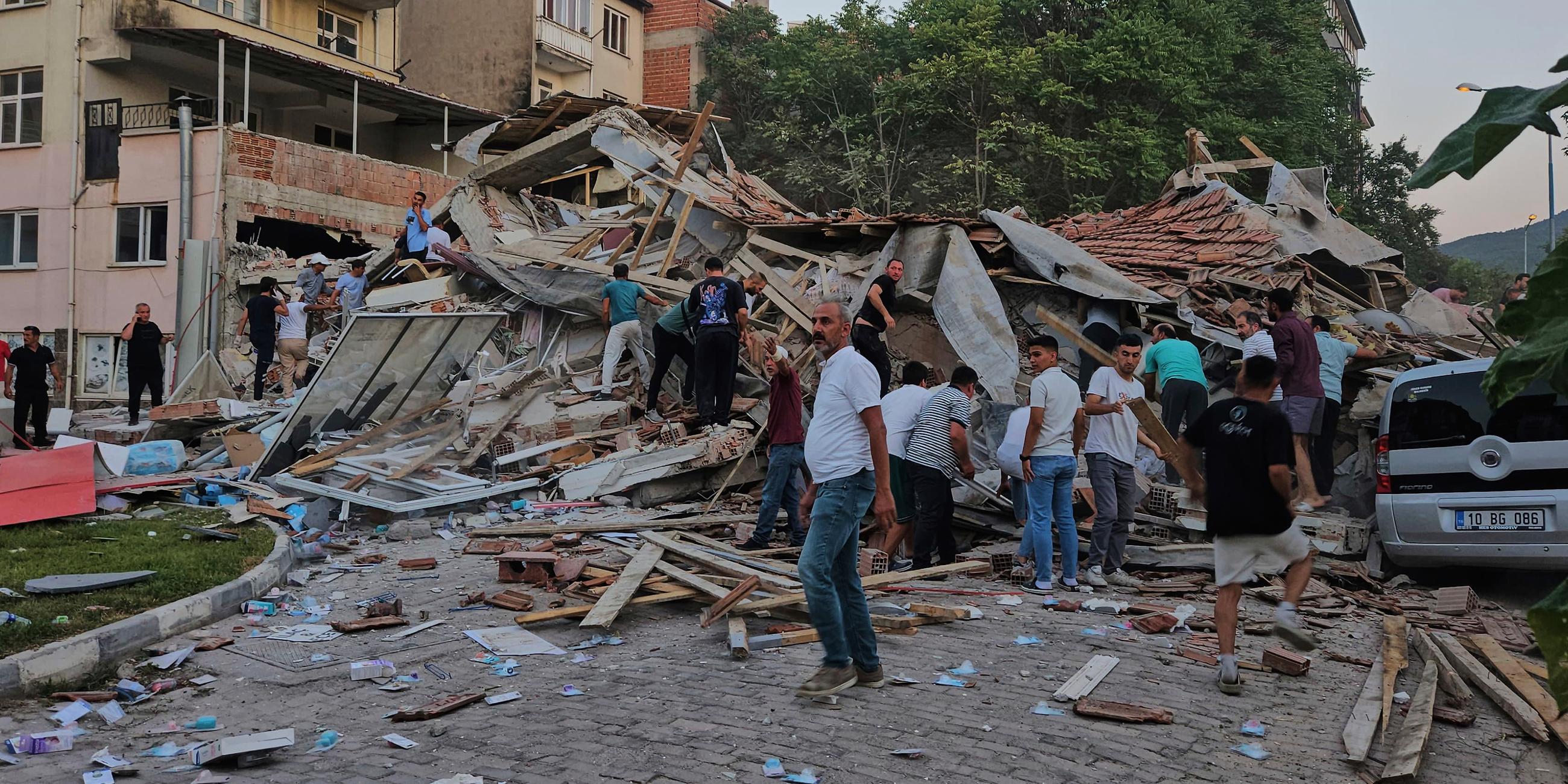 10.08.2025, Türkei, Sindirgi: Menschen beseitigen die Trümmer eines eingestürzten Gebäudes nach einem Erdbeben in Sindirgi in der Westtürkei.