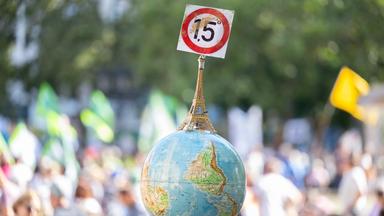 Auf einer Demo wird ein Globus mit einem Eifelturm und einem Schild mit der Aufschrift "1,5 Grad" hochgehalten.