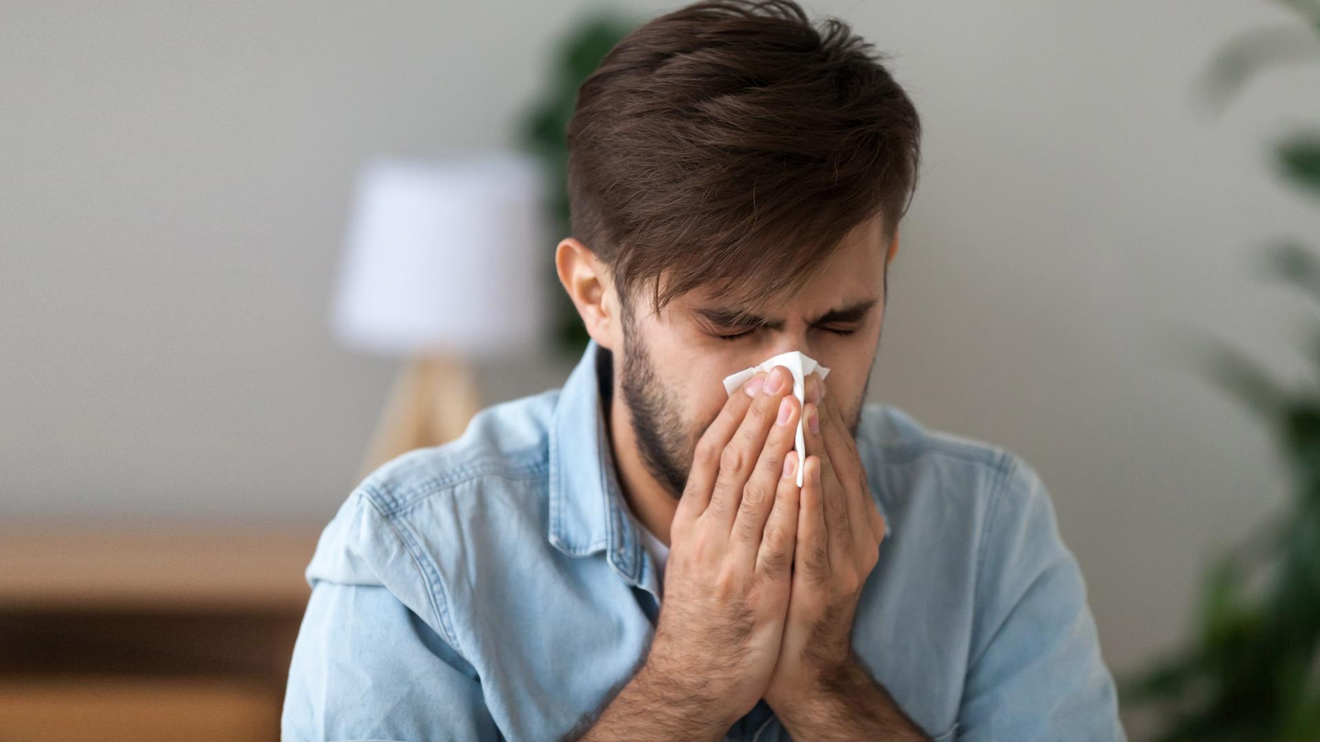 Ein Mann putzt sich mit einem Taschentuch die Nase.