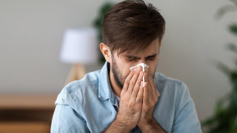 Ein Mann putzt sich mit einem Taschentuch die Nase.