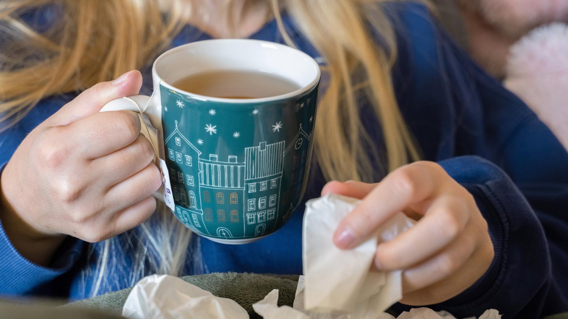 Symbolbild: Eine Frau trinkt Tee und hält ein Taschentuch in ihrer Hand. 
