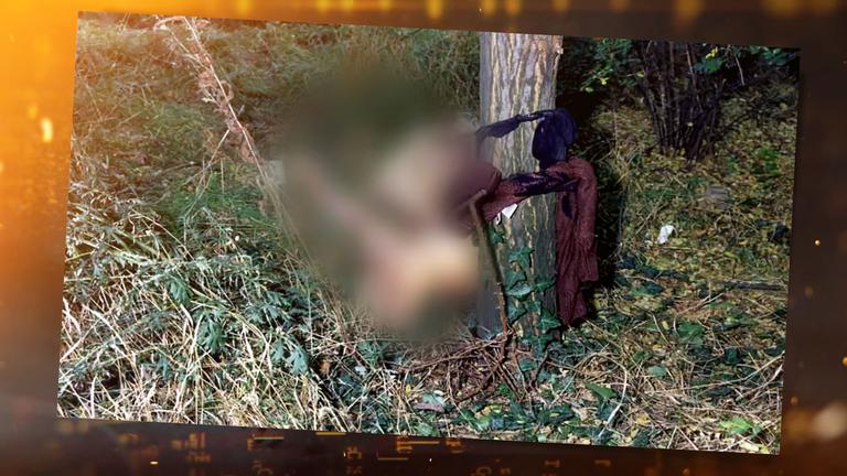 Tatort-Foto: Die unbekleidete Leiche einer jungen Frau in sitzender Position auf einer Wiese, ihre nackter Oberkörper ist mit einem blauen BH und einem braunen Pullover an einen Baum gebunden.