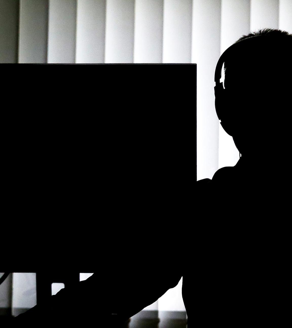 Symbolbild: Ein Beamter sitzt mit Kopfhörern vor einem Computer in einem Büro. 