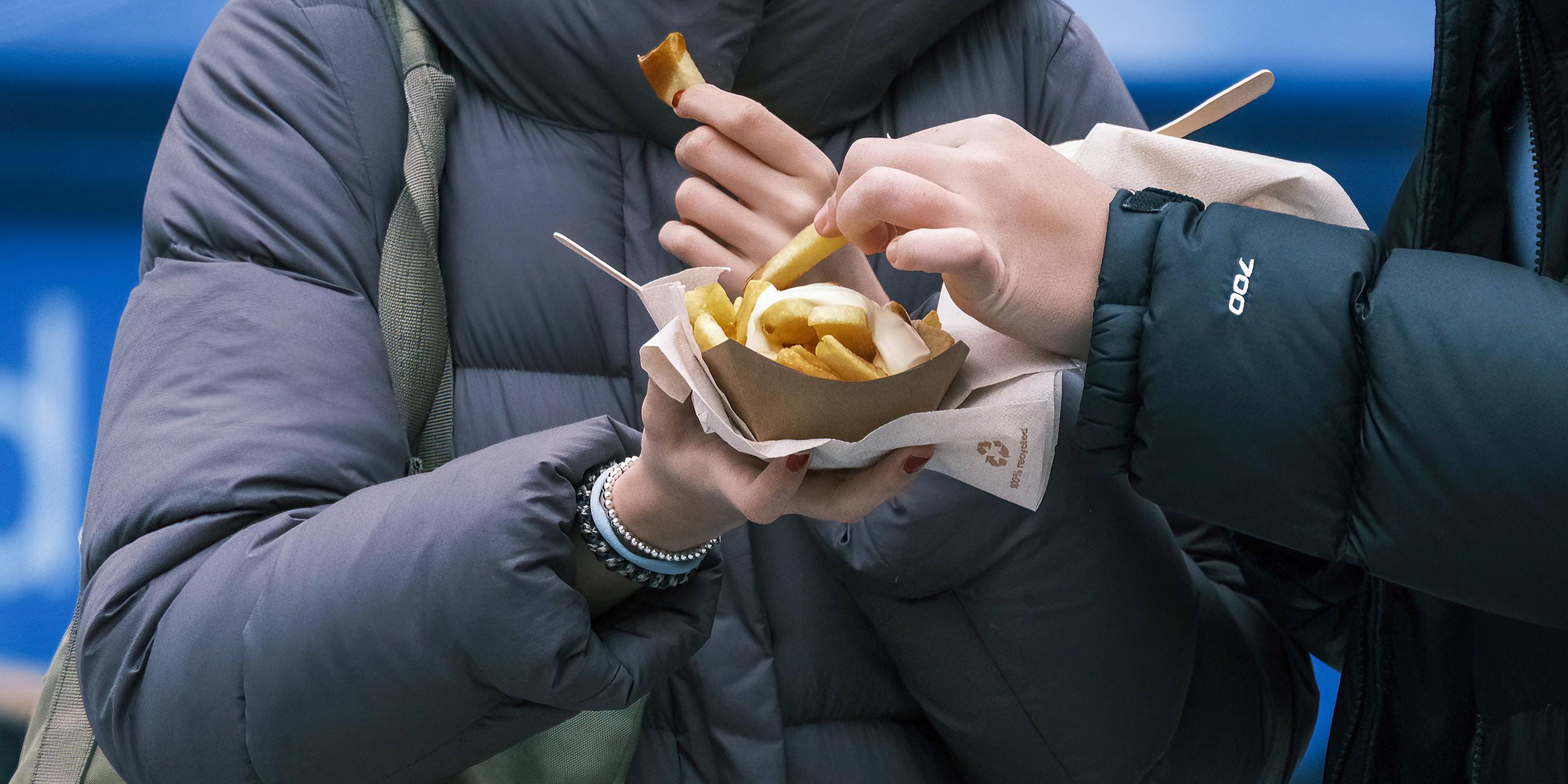 Junge Frauen essen Pommes mit Mayonnaise an einer Imbissbude
