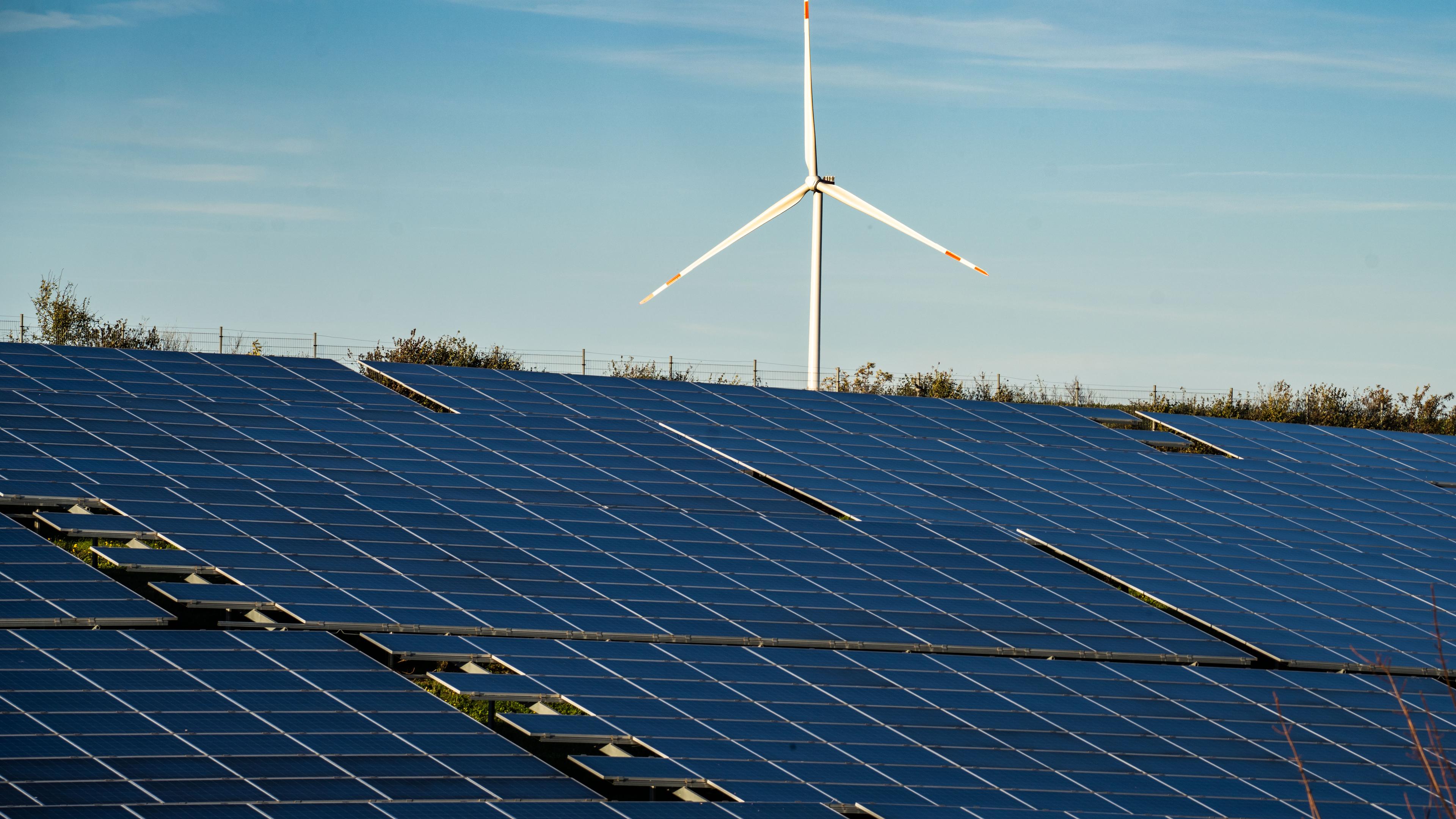 Ein Windrad oberhalb einer großflächigen Solaranlage auf einem Feld.