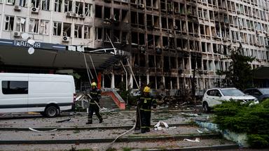 23.09.2026, Ukraine, Kiew: Rettungskräfte rollen vor einem Bürogebäude, das durch einen russischen Drohnenangriff beschädigt wurde, Feuerwehrschläuche auf.