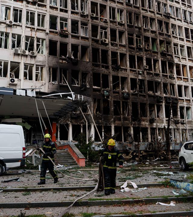 23.09.2026, Ukraine, Kiew: Rettungskräfte rollen vor einem Bürogebäude, das durch einen russischen Drohnenangriff beschädigt wurde, Feuerwehrschläuche auf.