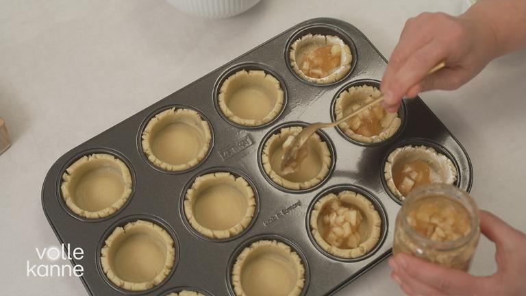 Frau füllt Apfelmatsche in Teig in Törtchenform