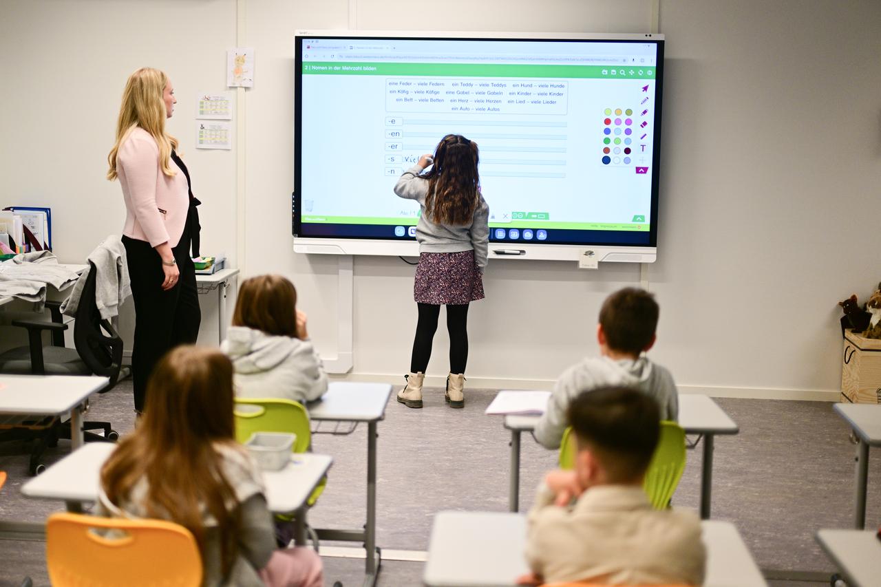 Ein Mädchen steht vorne an der digitalen Tafel und füllt etwas aus