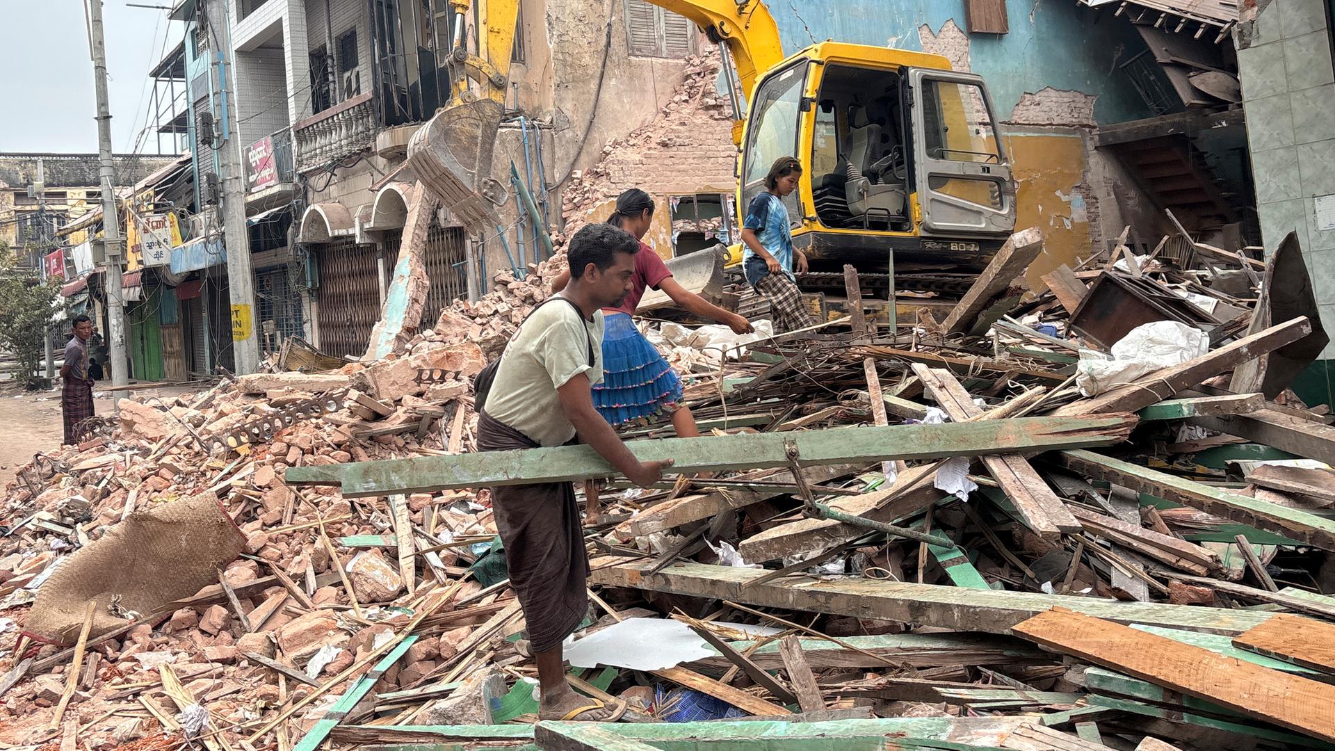 Drei Menschen, die Aufräumarbeit leisten. Im Hintergrund steht ein kleiner Bagger.