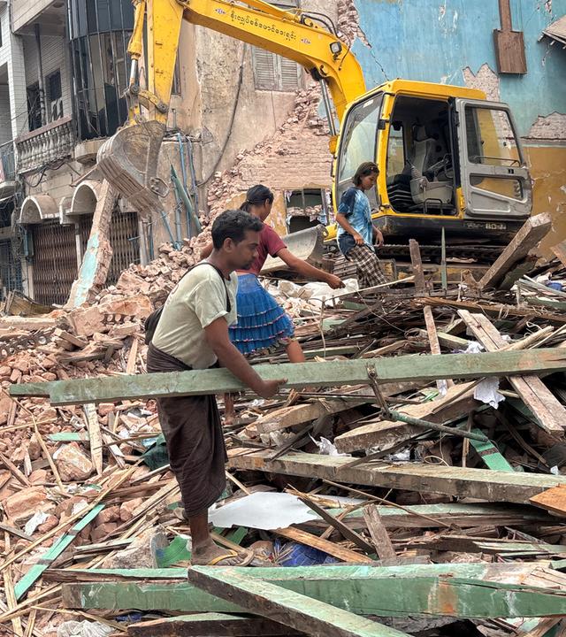 Drei Menschen, die Aufräumarbeit leisten. Im Hintergrund steht ein kleiner Bagger.