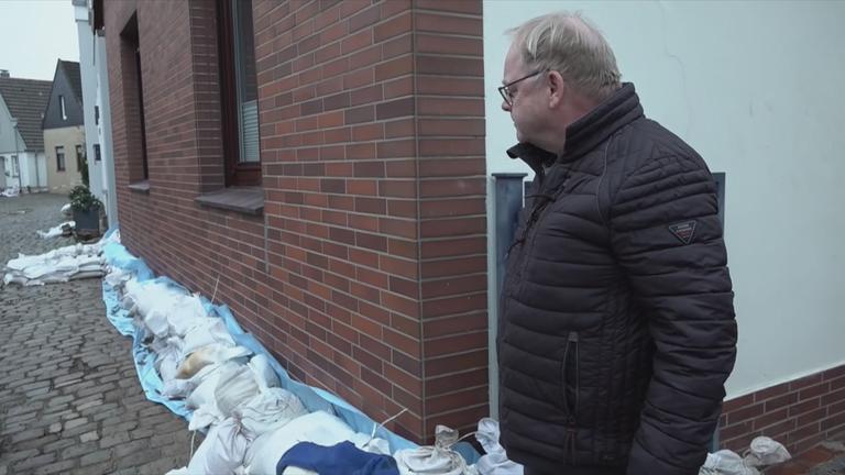 Auf dem Bild ist ein Mann zu sehen, der gerade sein Haus mit den Säcken davor anschaut.